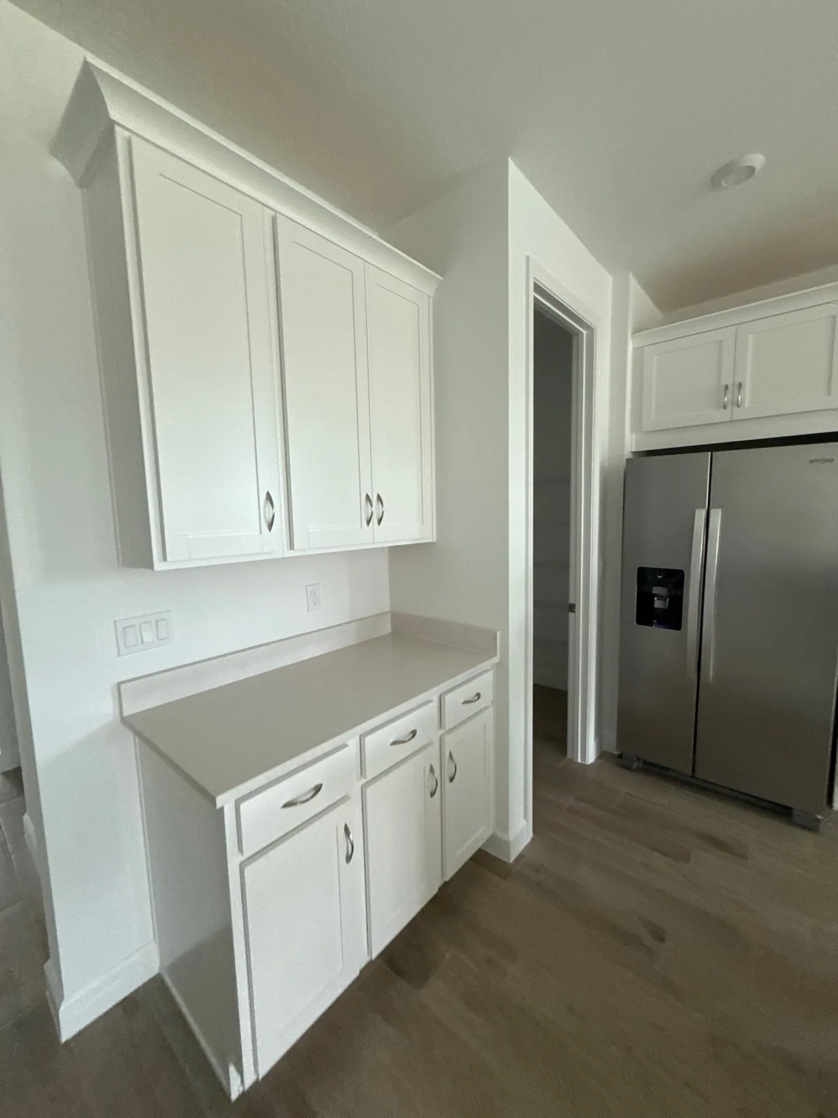 White refinished kitchen cabinets with silver handles beside a stainless refrigerator